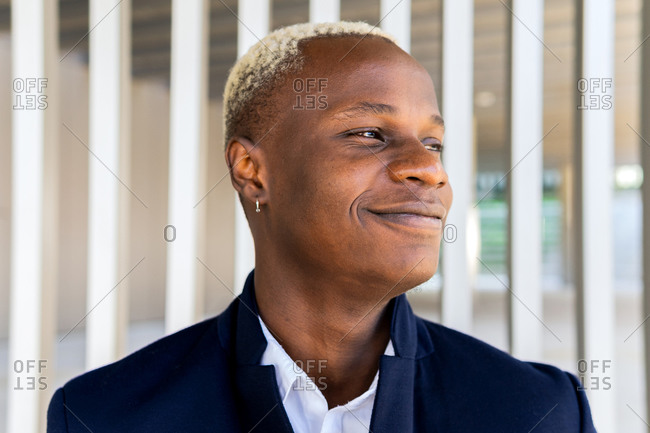 Satisfied African American male in casual outfit smiling and looking away on white background