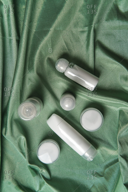 High angle of assorted plastic bottles and jars of skincare products arranged on green fabric background