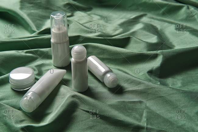High angle of assorted plastic bottles and jars of skincare products arranged on green fabric background