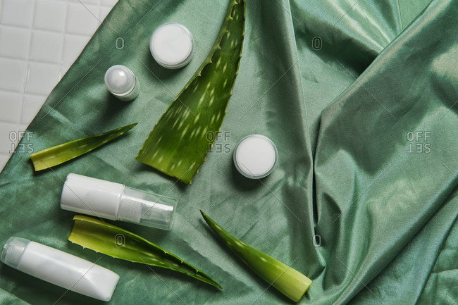 From above of arrangement of aloe vera leaves and various cosmetic products on green fabric