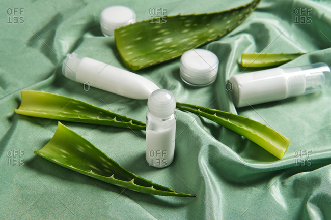 From above of arrangement of aloe vera leaves and various cosmetic products on green fabric