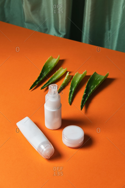 Top view of facial skin care products in white plastic jars and leaves of aloe vera plant placed on orange background in studio