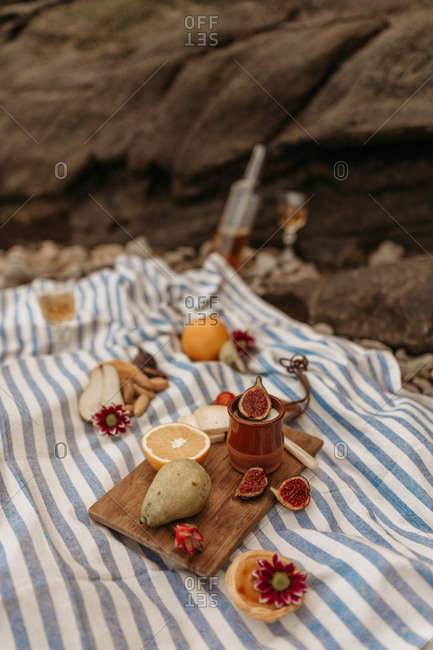 High angle of appetizing assorted food on wooden cutting board arranged on blanket placed near river for picnic