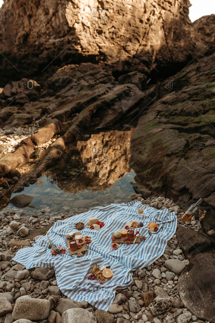 High angle of appetizing assorted food on wooden cutting board arranged on blanket placed near river for picnic