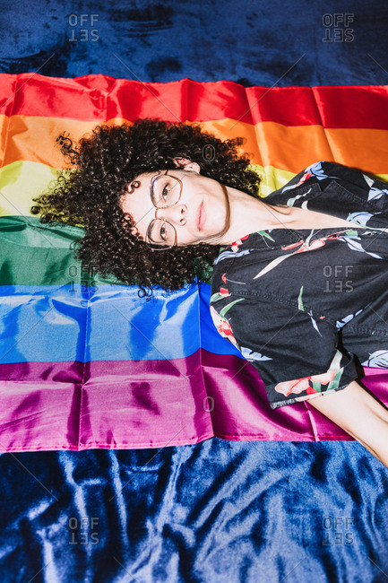 From above of calm upside down female in eye glasses lying on colorful LGBT flag in bedroom