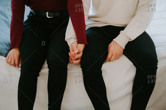 High angle of crop couple resting on bed and tenderly holding hands while spending weekend together