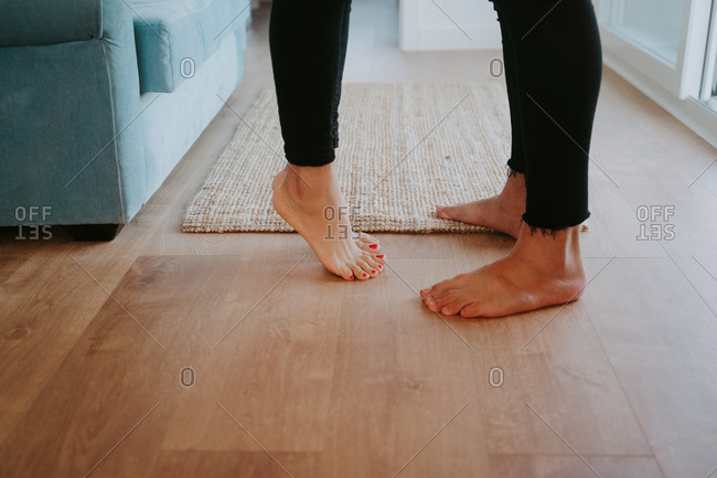 Barefoot legs of crop unrecognizable couple standing on wooden floor in cozy room at home