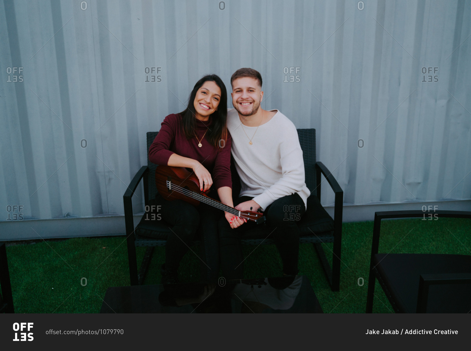 Portrait of tranquil couple sitting on backyard of container house and playing ukulele while enjoying music in evening