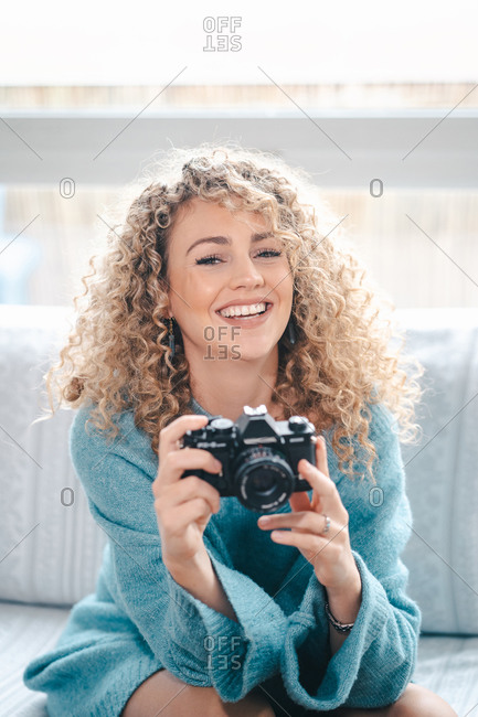 Charming female with curly hair taking picture on photo camera in bright apartment