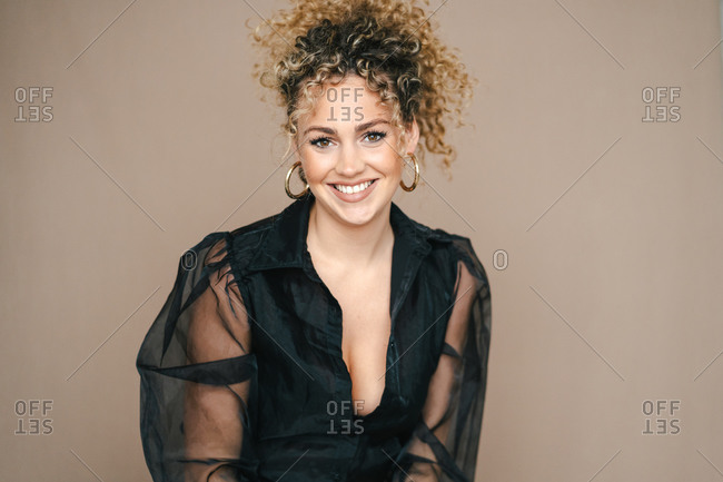 Optimistic female with curly hair smiling in studio and looking at camera