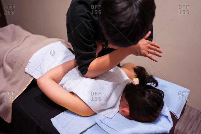 Crop unrecognizable masseur putting white towel on client covered with blanket while doing rehabilitation massage in professional salon