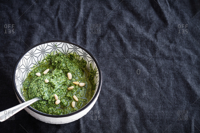 From above of ceramic bowl with fresh aromatic green pesto sauce with pine nuts placed on black cloth
