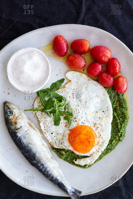 From above fried egg served with salty fish and marinated tomatoes and garnished with pesto sauce