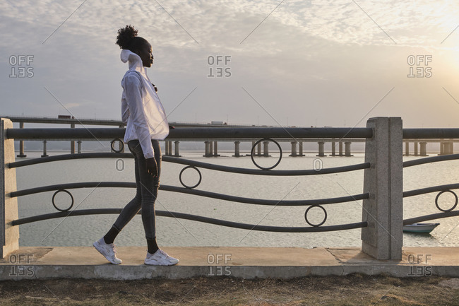 Full body side view of carefree young African American female student in casual clothes standing near railing against urban seafront
