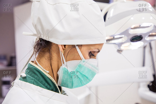 Side view of female doctor wearing medical protective mask and uniform working in bright modern hospital