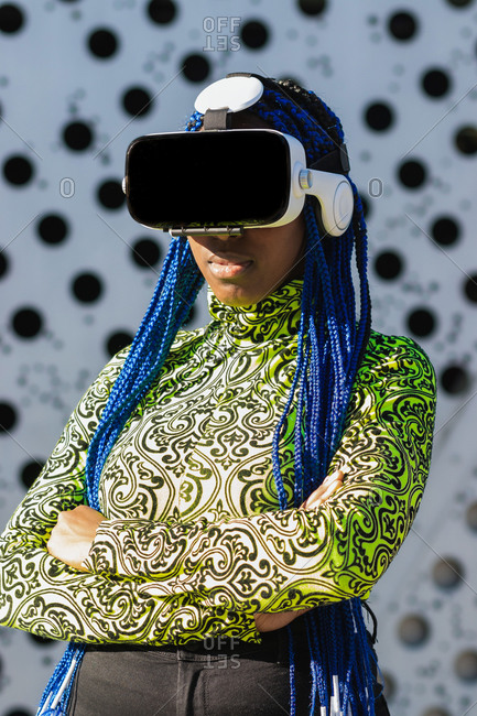 Side view of African American female with blue hair standing in street in VR goggles while experiencing virtual reality