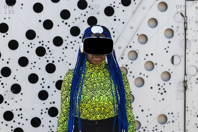 African American female with blue hair standing in street in VR goggles while experiencing virtual reality