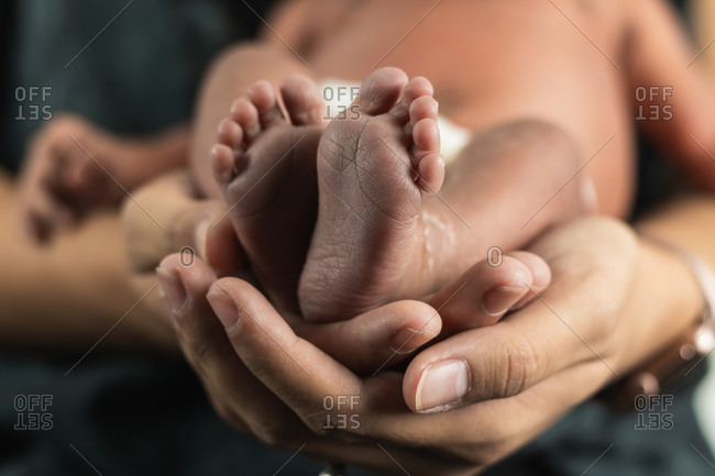Closeup crop unrecognizable woman holding tiny feet of anonymous baby