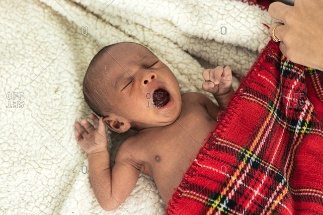 Tranquil adorable newborn baby lying on soft red tartan blanket with open mouth yawning
