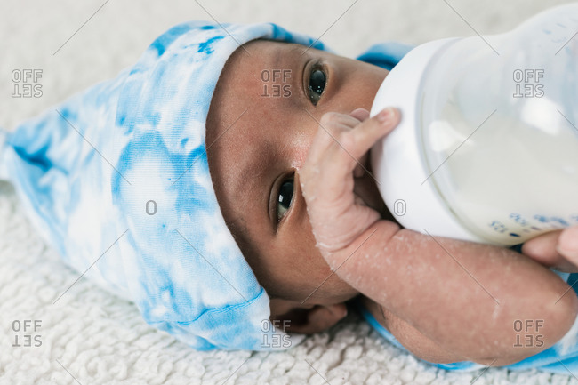 Cropped unrecognizable mother feeding tranquil adorable newborn baby with milk bottle wrapped on blue cozy blanket