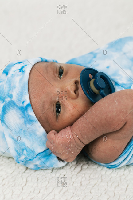 Tranquil adorable newborn baby lying wrapped on blue cozy blanket using pacifier