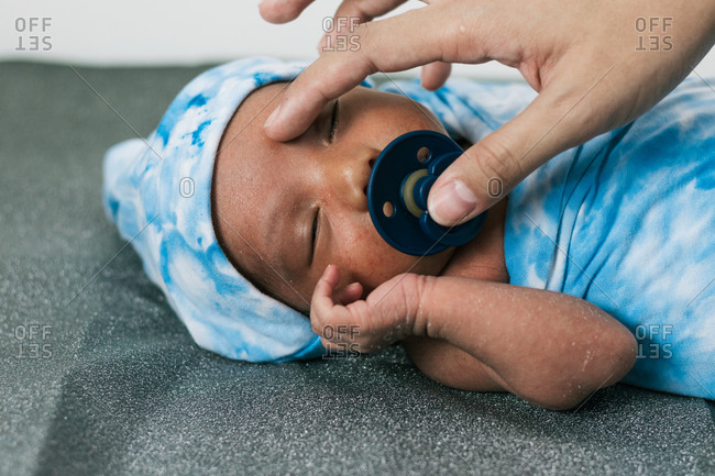 Cropped unrecognizable mother hand touching tranquil adorable newborn baby lying wrapped on blue cozy blanket using pacifier