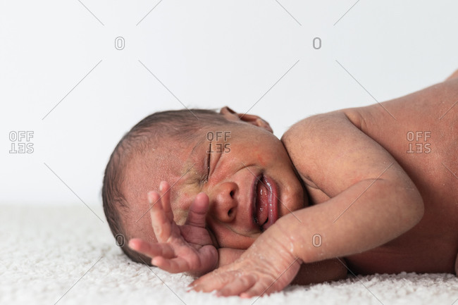 Upset crying newborn baby lying on soft blanket with eyes closed