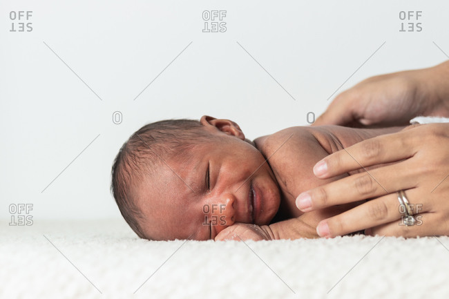 Crop unrecognizable woman hand holding tiny sleepy newborn baby lying on soft blanket