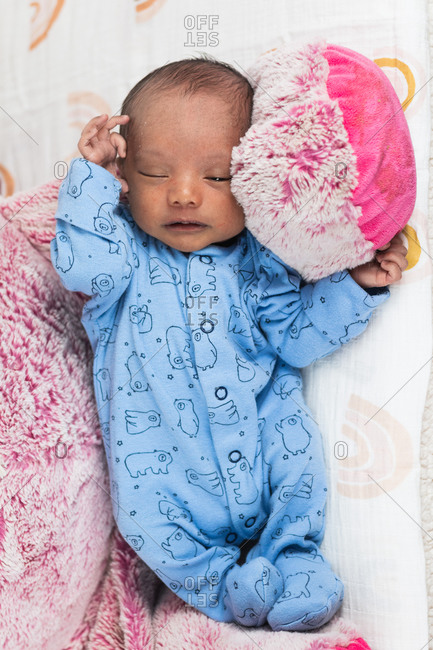 From above tranquil adorable newborn baby lying sleeping on big toy on cozy blanket