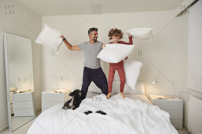 Playful father and son fighting on bed with soft pillows while jumping and having fun