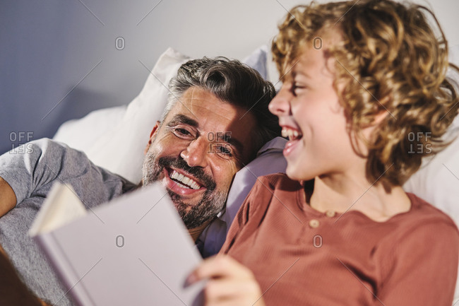Peaceful man and boy lying on bed and reading interesting story in book together