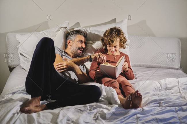 Peaceful man and boy lying on bed and reading interesting story in book together