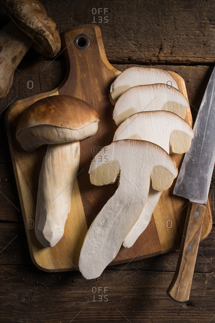 From above composition of raw whole and sliced porcini or cep mushrooms with knife and cutting board on wooden rustic table