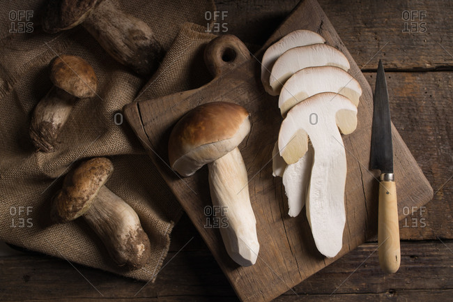 From above composition of raw whole and sliced porcini or cep mushrooms with knife and cutting board on wooden rustic table
