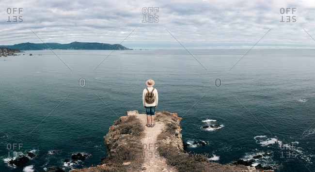Unrecognizable male traveler standing on rocky hill and observing wonderful scenery of sea under cloudy sky