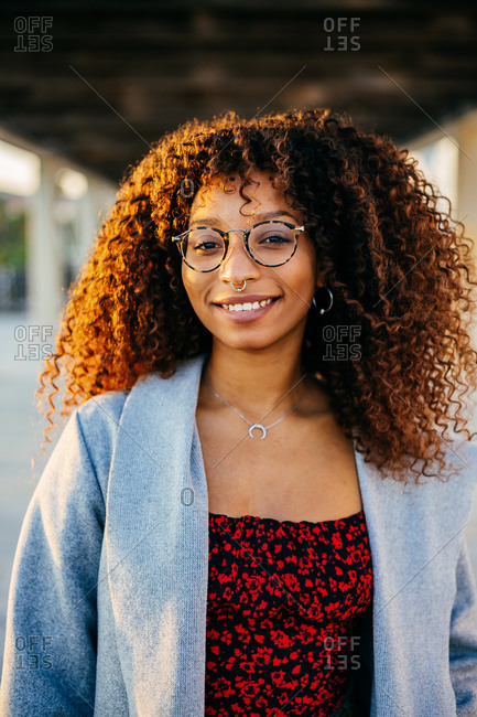 Young black female in trendy outfit and glasses looking at camera while standing under roof on city street