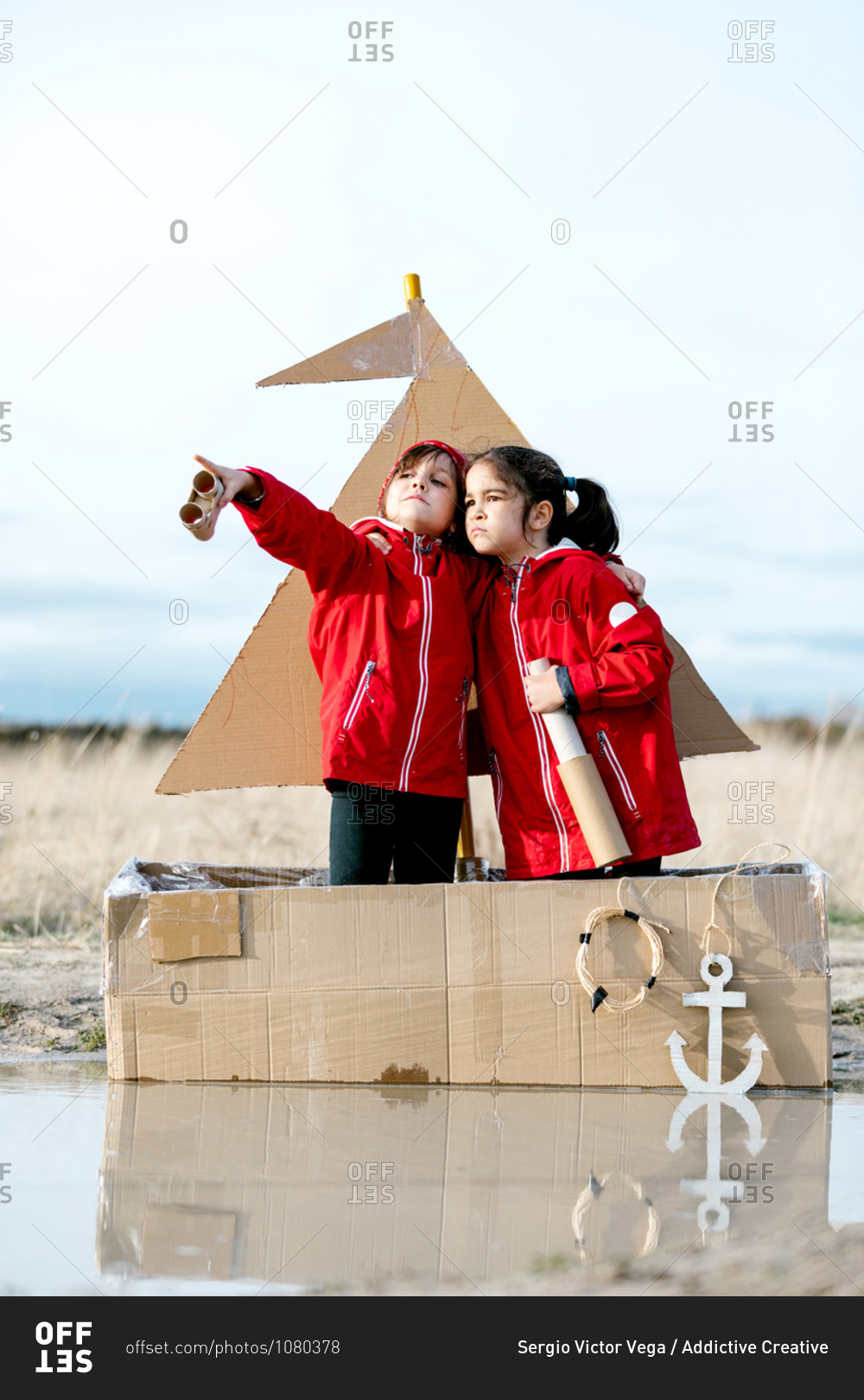 Side view of cheerful kids with handmade spyglass standing in handmade cardboard boat and playing