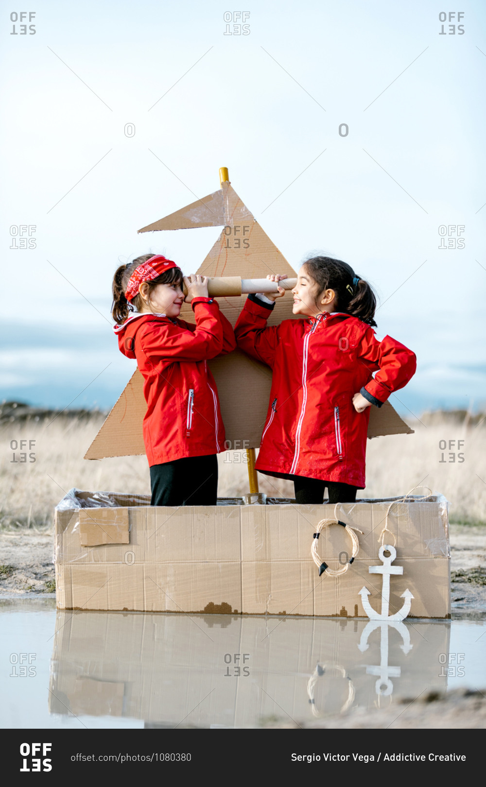 Side view of cheerful kids with handmade spyglass standing in handmade cardboard boat and playing