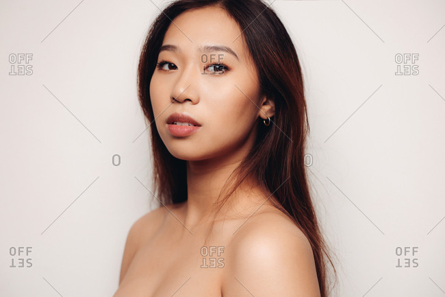 Portrait of naked young Chinese woman looking at camera over white background