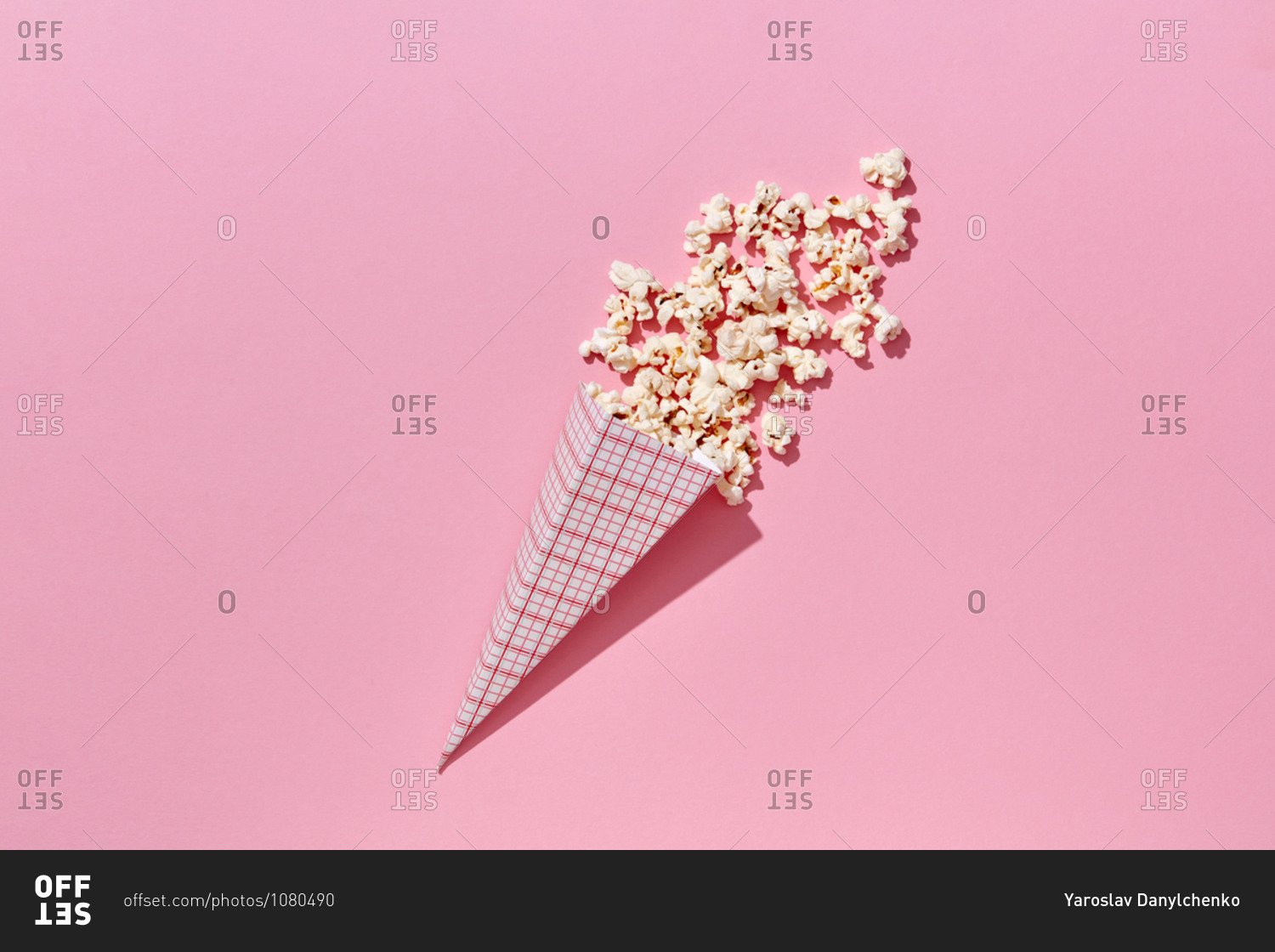 Tasty cooked classic popcorn in paper cone on pink background