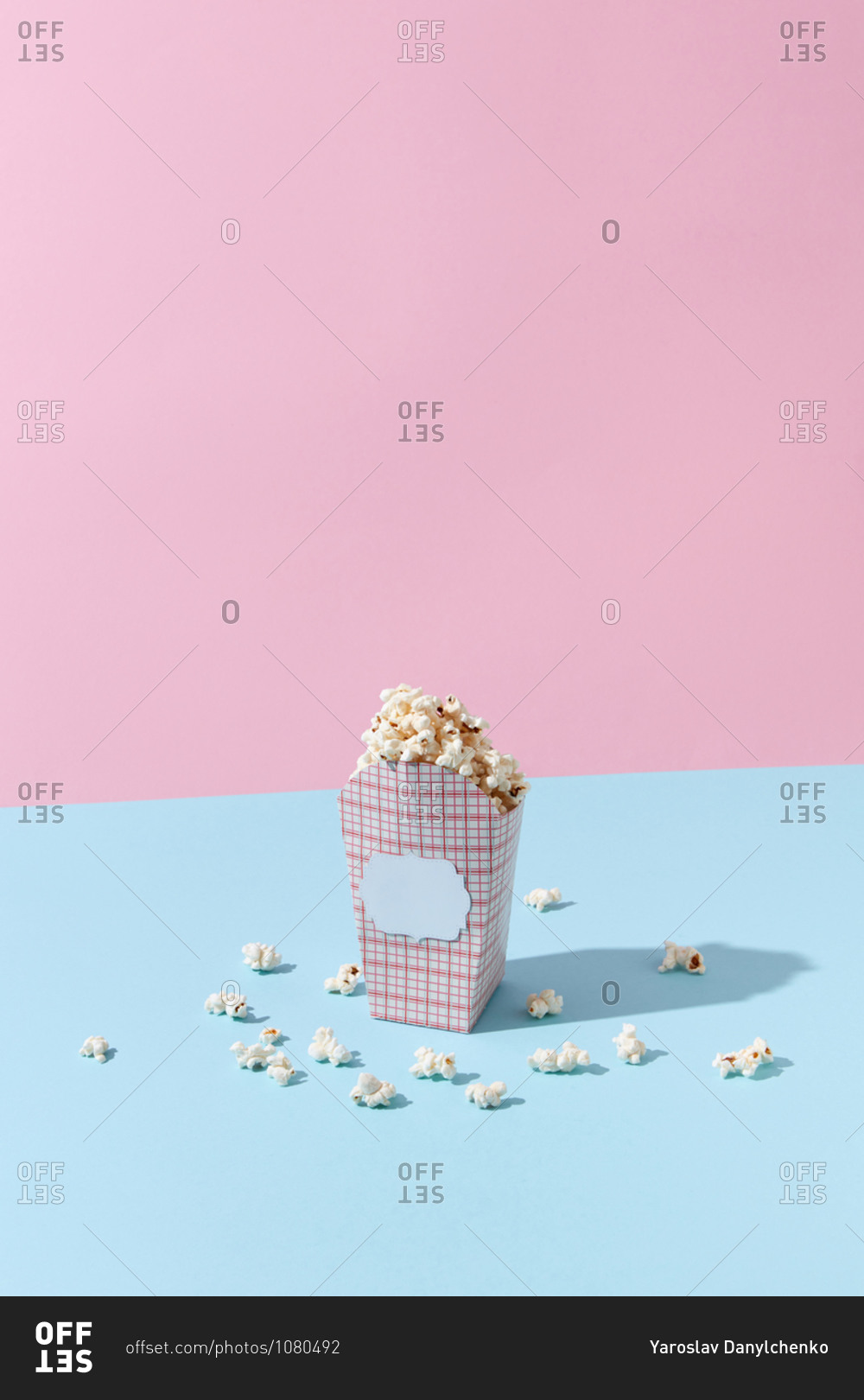 Delicious cooked classic popcorn in carton container on pink and blue background, copy space