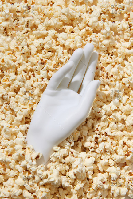 Plaster white hand in cooked appetizing heap of popcorn