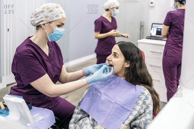 Woman sitting in dentist\'s chair putting on teeth covers.