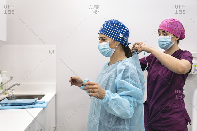 Woman wearing face mask and hair net helping her coworker in a dental clinic.