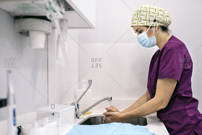 Woman wearing face mask and hair net working in modern dental clinic washing her hands.
