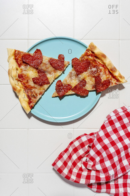 Pizza with pepperoni in heart shapes on blue plate- white tiles and white and red checkered napkin