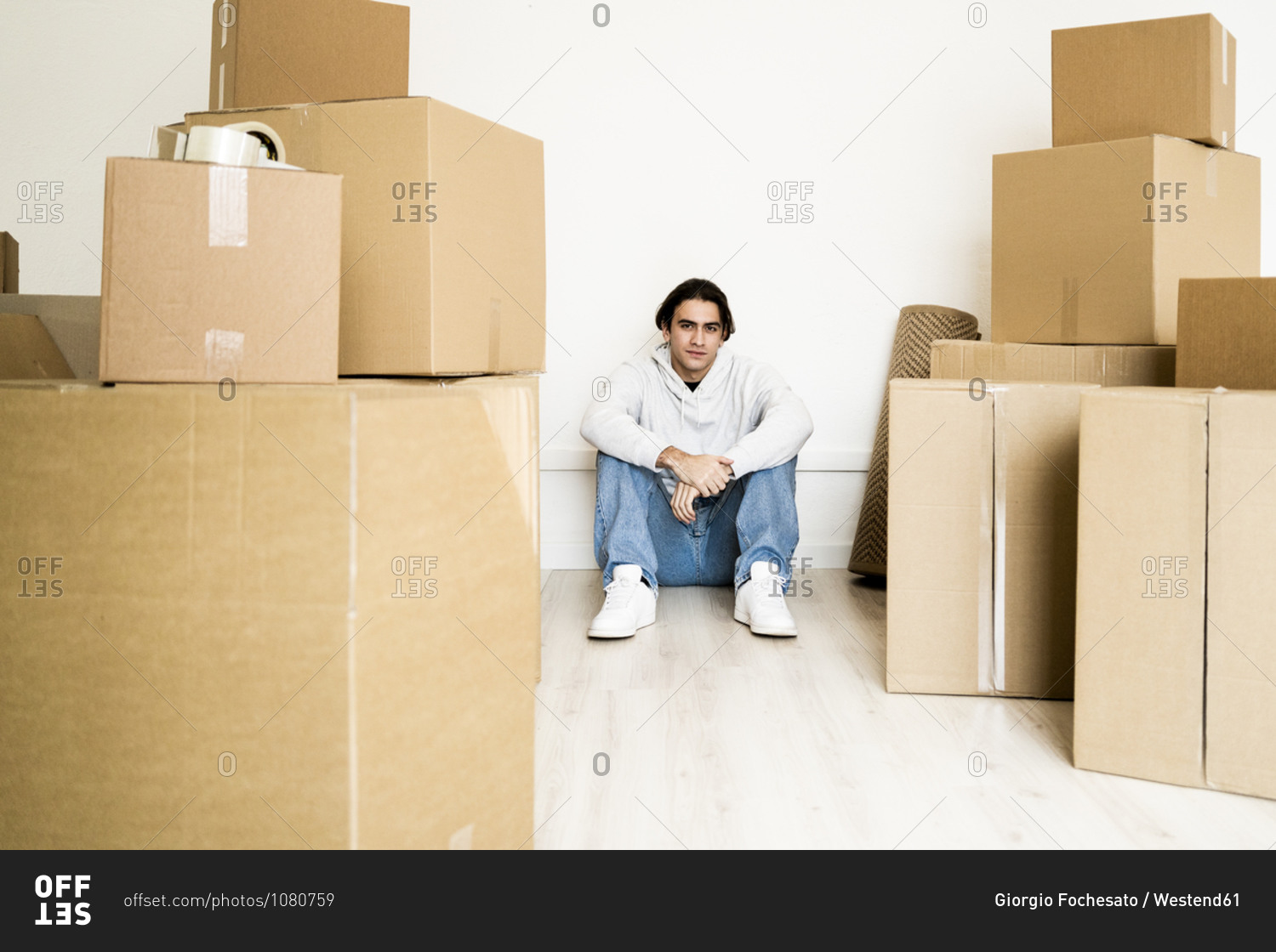 Man sitting amidst cardboard boxes on floor in living room of new house