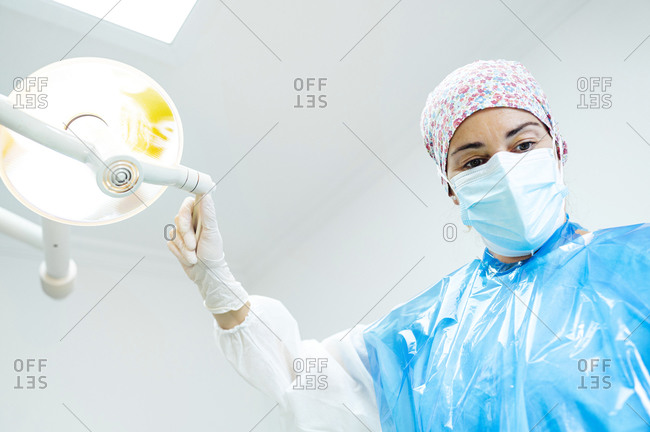 Dental doctor adjusting illuminated electric lamp while standing at clinic during Covid-19