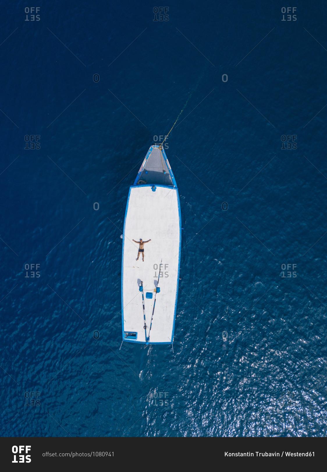 Aerial view of shirtless man relaxing on roof of boat drifting in blue ...