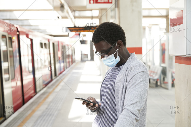 Male commuter wearing protective face mask while using mobile phone at railroad station